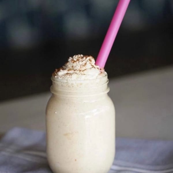 Creamy milkshake in a mason jar, topped with whipped cream, cinnamon, and a pink straw.