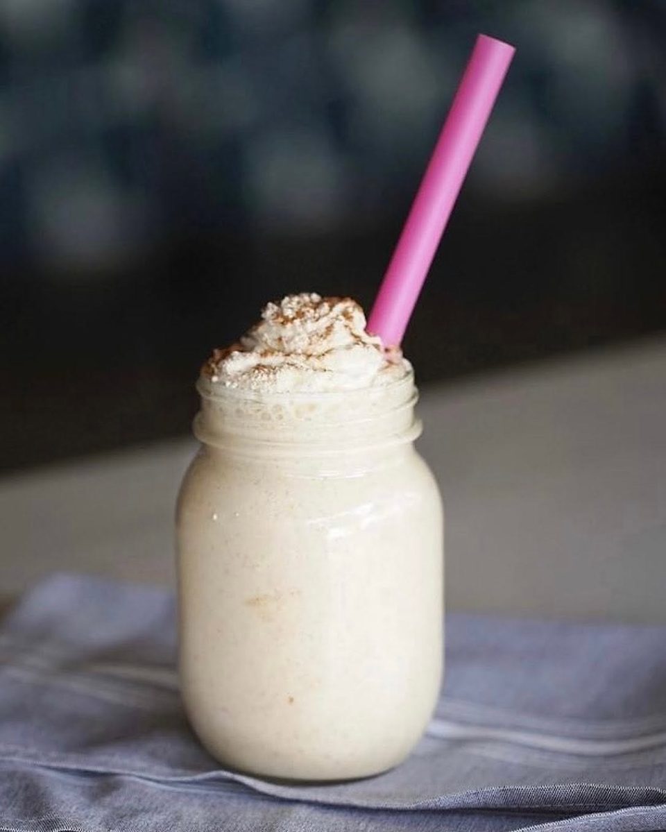 Creamy milkshake in a mason jar, topped with whipped cream, cinnamon, and a pink straw.