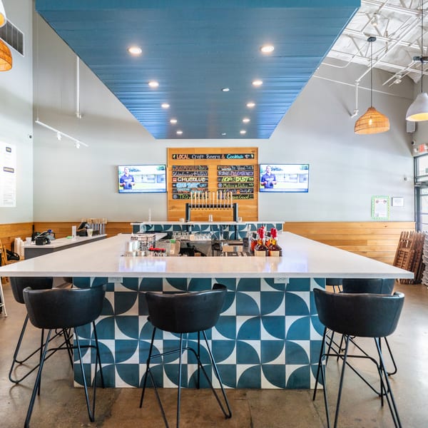 A modern restaurant interior with a long bar featuring blue and white patterned tiles and black bar stools.