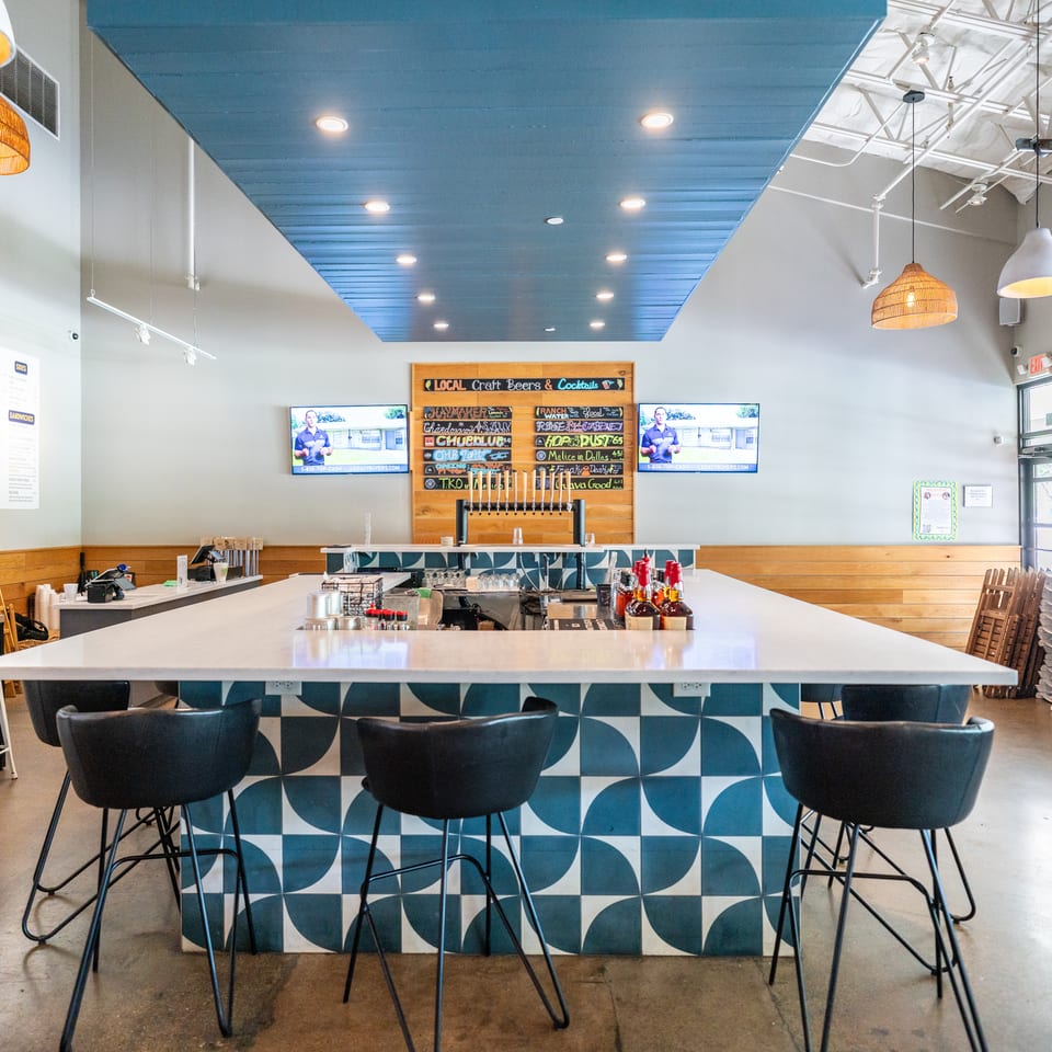 A modern restaurant interior with a long bar featuring blue and white patterned tiles and black bar stools.