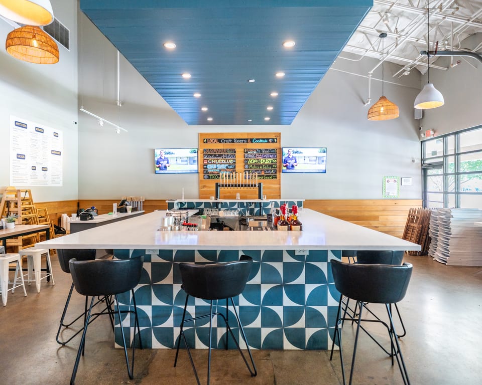 A modern restaurant interior with a long bar featuring blue and white patterned tiles and black bar stools.