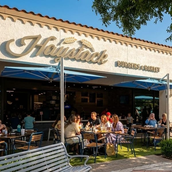 Diners enjoy outdoor patio seating under blue umbrellas at Haystack Burgers & Barley restaurant.