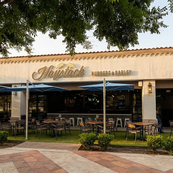 Haystack Burgers & Barley restaurant exterior with outdoor patio seating under blue umbrellas.