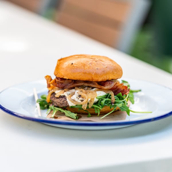 Gourmet burger with bacon, caramelized onions, cheese, and arugula on a white plate.