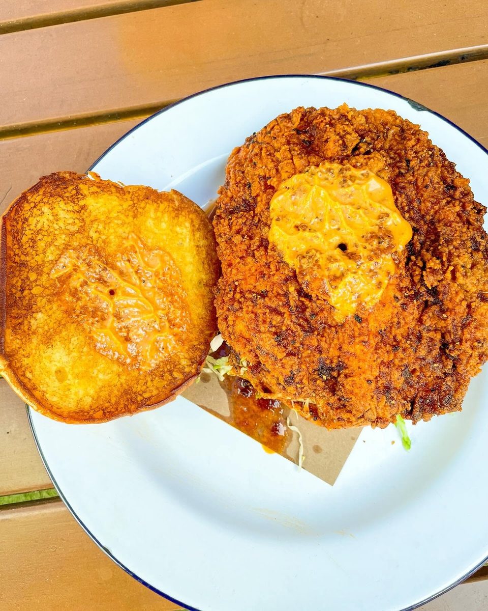 Crispy fried chicken sandwich with sauce on a toasted bun, served on a white plate.
