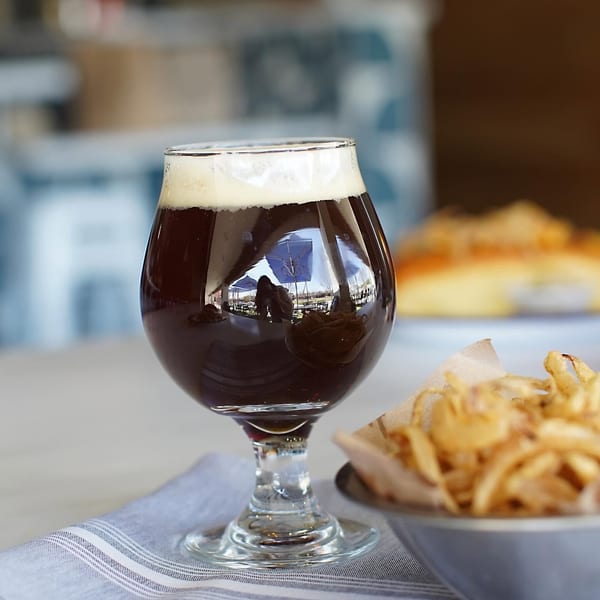 Dark beer in a stemmed glass with a bowl of crispy fried onions on a striped napkin.