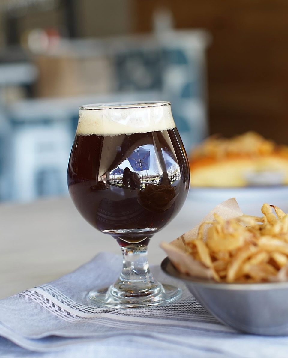 Dark beer in a stemmed glass with a bowl of crispy fried onions on a striped napkin.