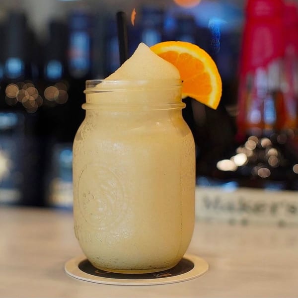 A frozen drink in a mason jar with an orange slice and straw on a coaster.