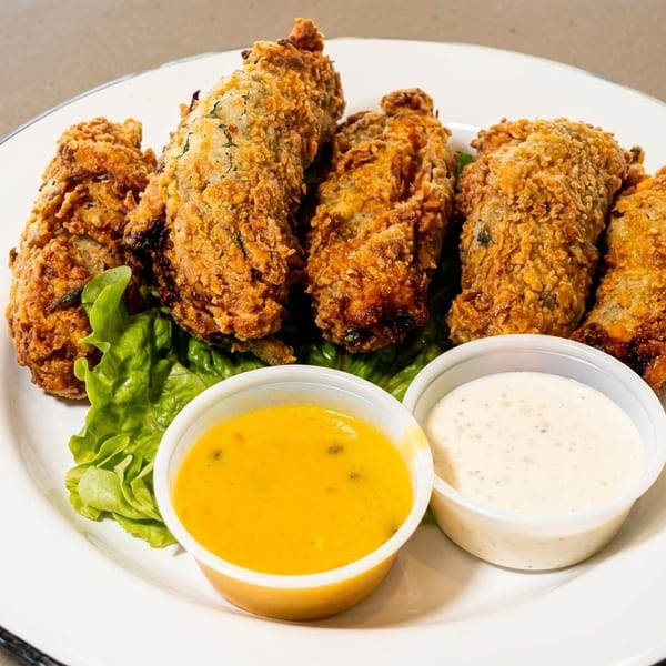 Crispy fried oysters on lettuce with two dipping sauces on a white plate.