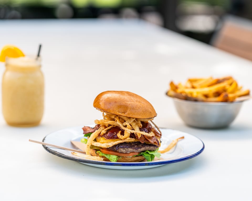 A bacon cheeseburger with crispy onions, a side of fries, and a smoothie on a white table.