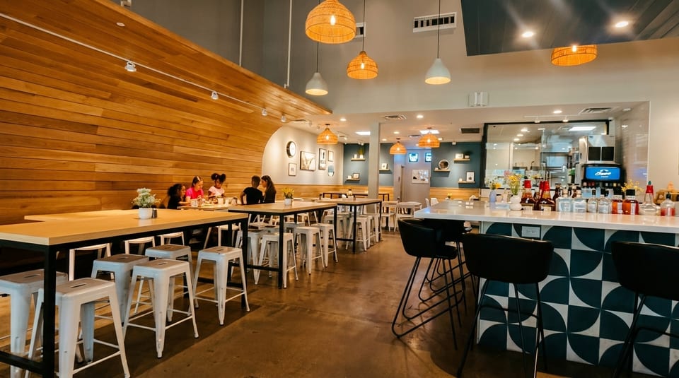 A modern restaurant interior with wooden walls, hanging lights, and a bar with patterned tiles.